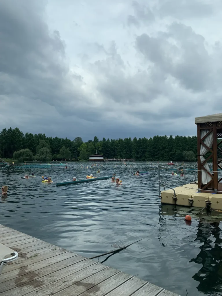 Swimmers with pool noodles in the open water of Lake Hévíz on a cloudy day